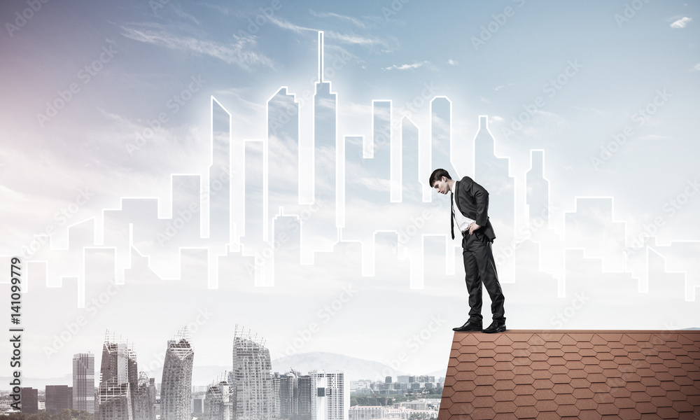 Businessman looking down from roof and modern cityscape at backg