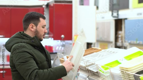 The adult young guy chooses the goods in the mall. People in-store. Shelves with goods. House hold goods. Kitchen ware. Kitchen box. Male in shopping center. Shopper indoor. Furniture store. photo