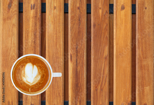 Top view of a coffee with heart pattern in a white cup on wooden plank background, latte art