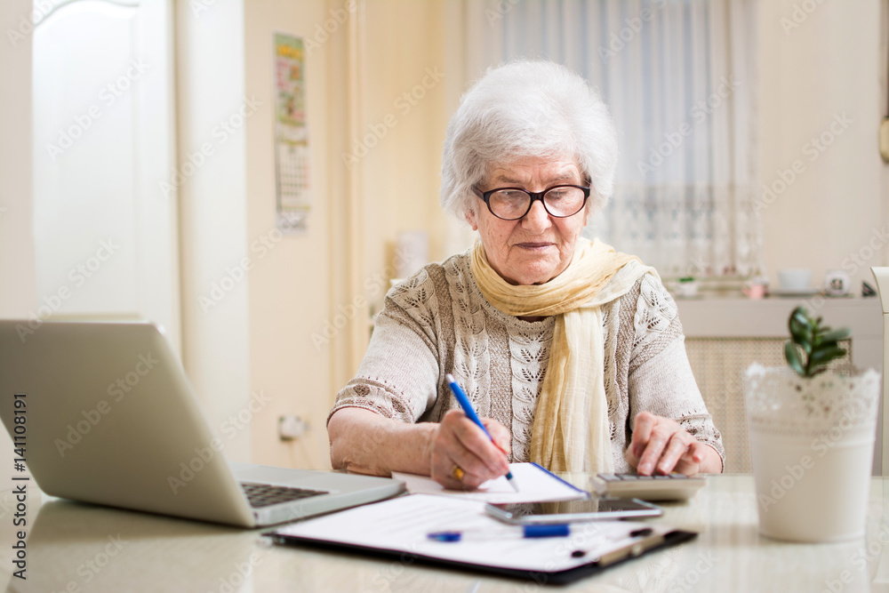Senior businesswoman calculating taxes at home. Senior businesswoman calculating taxes at home.