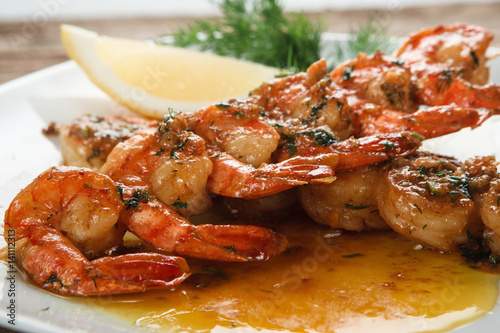 Tasty Japanese seafood. Fried spicy shrimps on wooden skewers served on plate with herbs and lemon, close up view. Mediterranean food