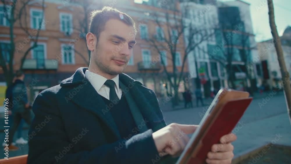 Young, attractive businessman sitting on a bench using a tablet computer