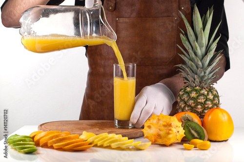 Adult pouring an orange juice into a glass from a jar. Composition a ripe tropical fruits photo