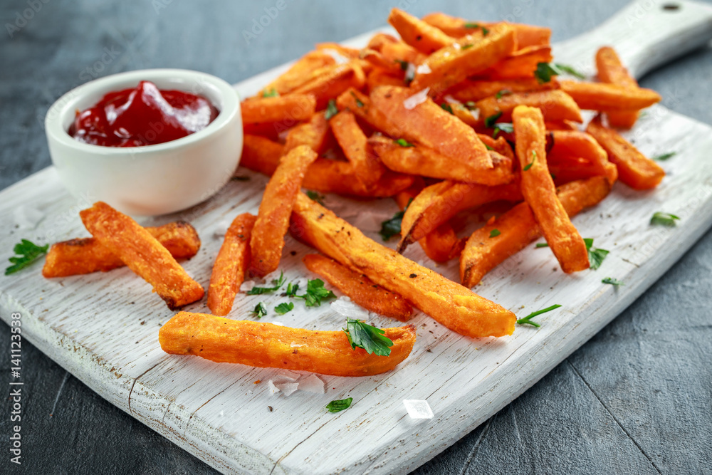 Healthy Homemade Baked Orange Sweet Potato Fries with ketchup, salt, pepper on white wooden board Healthy Homemade Baked Orange Sweet Potato Fries with ketchup, salt, pepper on white wooden board