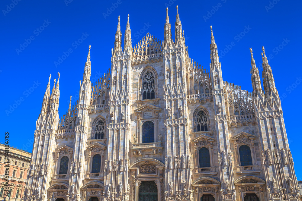 Gothic cathedral facade in Piazza Duomo square of Famous Milan Dome church against a blue sky at midday.Milan Cathedral is a popular landmark and city icon.