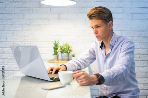 Принти на полотні Young man with cup of coffee using laptop at home.