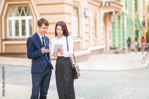 Beautiful young business woman and handsome businessman in formal suits are using a digital tablet in city background.