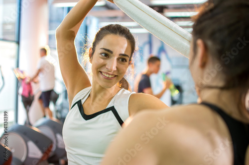 Happy young woman with towel in hands talking to her friend in a gym.