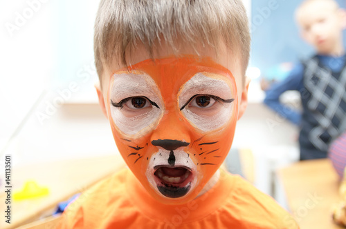 Make up artist making tiger mask for child.Children face painting. Boy  painted as tiger or ferocious lion. Preparing for theatrical performance. Boy actor playing role. Tiger mask face
