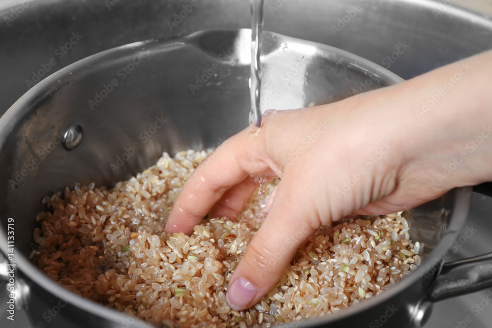 Female hand washing raw brown rice in saucepan Female hand washing raw brown rice in saucepan