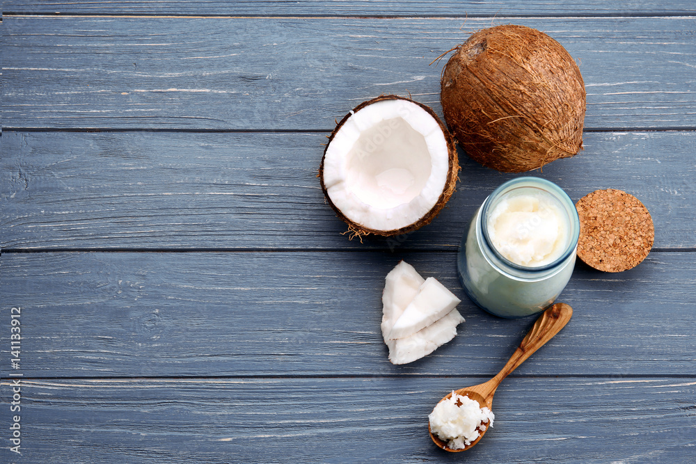 Spoon and glass jar with fresh coconut oil on wooden background
