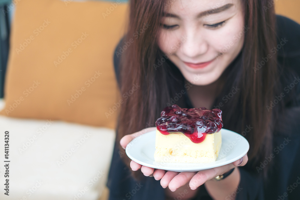 A beautiful asian woman holding blueberry cheese cake with feeling happy and good lifestyle in modern cafe A beautiful asian woman holding blueberry cheese cake with feeling happy and good lifestyle in modern cafe