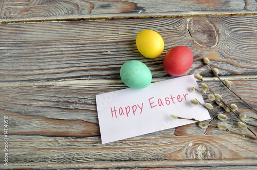Пасхальные цветные яйца и верба  являются символом праздника.  Яйца, письмо с пожеланием и верба находятся на деревянном столе
 