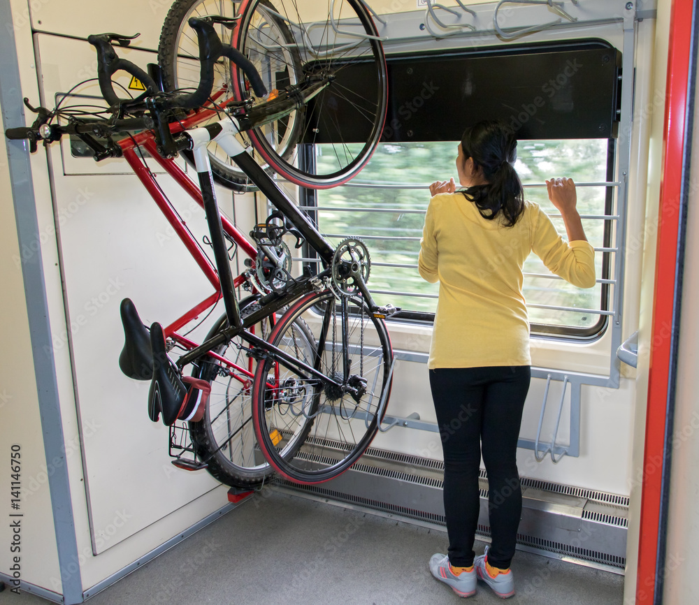 Bike hanging on the rack in the train. Transport bicycles in the  wagon.Woman traveling on a train with a bicycle. Photos | Adobe Stock