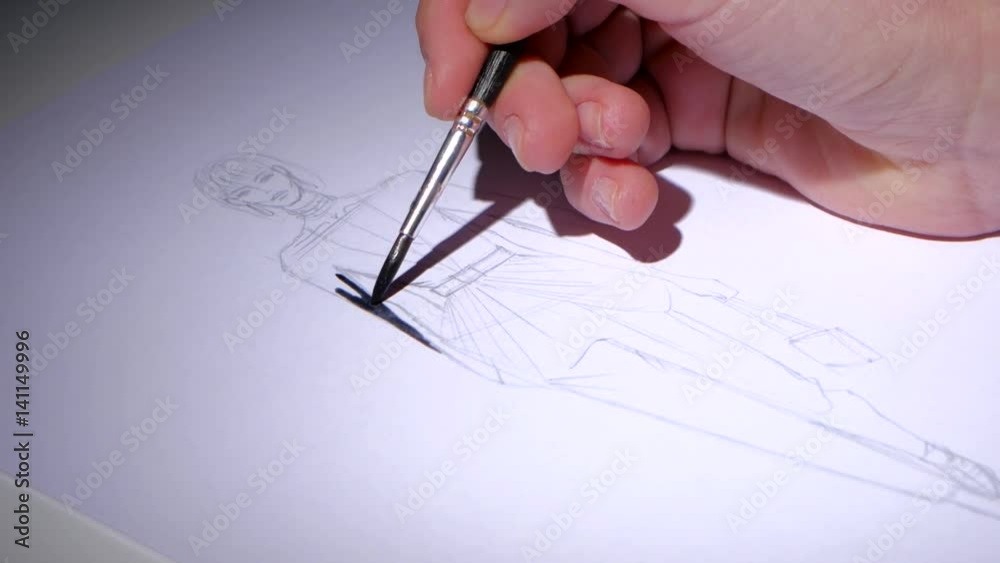Designer colors the sketch of the dress with black paint. Close up Designer colors the sketch of the dress with black paint. Close up