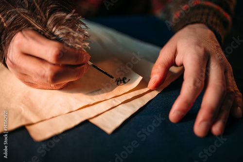 Male hands writes with a feather on vintage paper