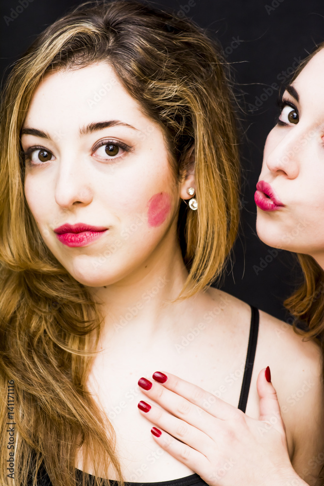 Two beautiful women where one of them is giving a kiss on the cheek to the other over Black Background Two beautiful women where one of them is giving a kiss on the cheek to the other over Black Background