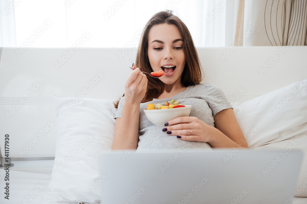 Side view of pregnant woman using tablet and eating fruits Side view of pregnant woman using tablet and eating fruits