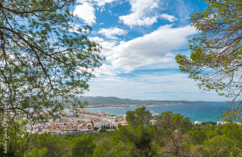 View from the hills into St Antoni de Portmany & surrounding area in Ibiza.  Clearing November day in the bay. Wide angle view through trees from high point on nearby hillside.
