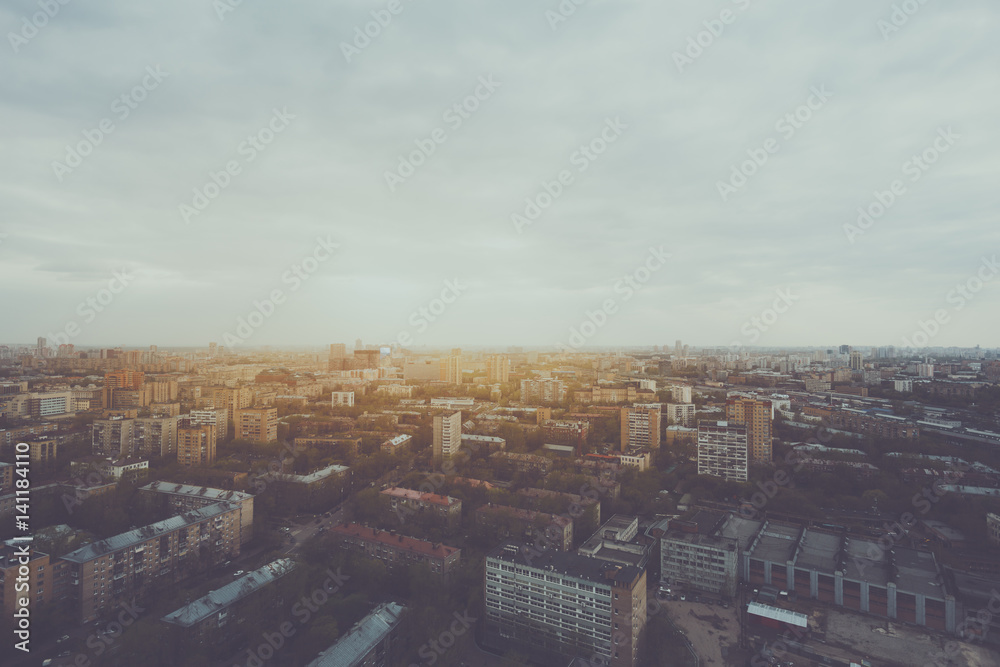 Wide angle view from high above of metropolitan city: multiple residential districts and houses, cloudy sky, trees and parks, industrial zone, road hazy horizon on sunset or sunrise