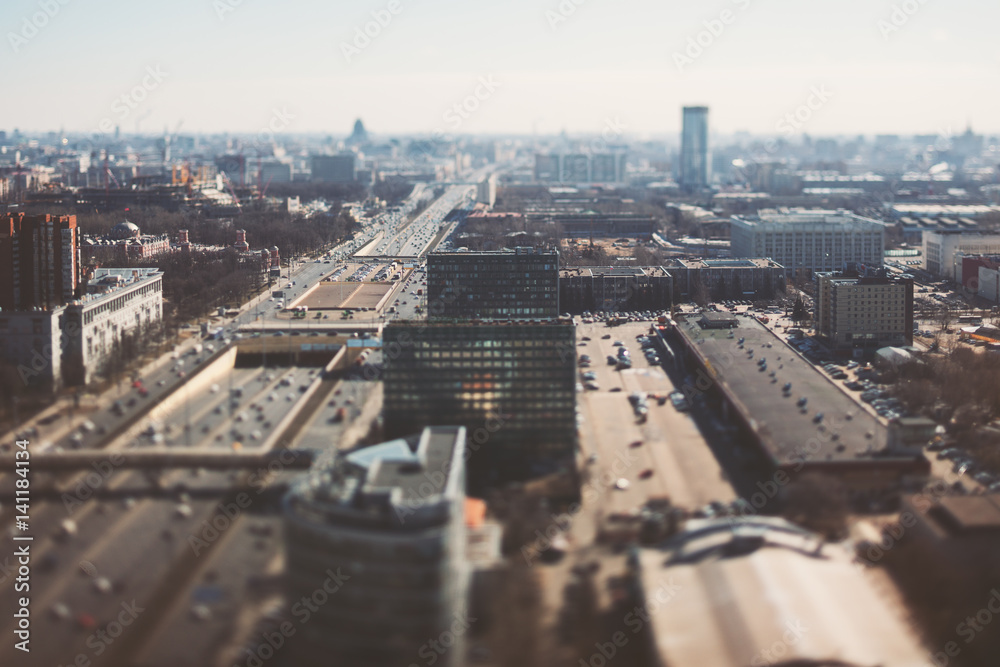 Fototapeta premium True tilt shift shooting of highway in metropolis from high point: multiple residential and office buildings, road intersection in focus with many cars on busy streets of the city, crosstown traffic