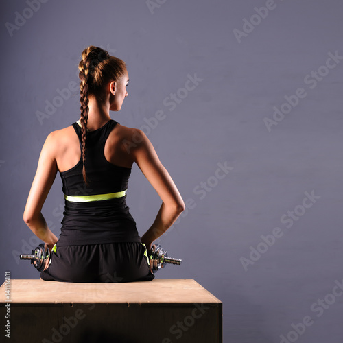 Fit young woman doing shoulder raises with dumbbells, isolated ongray background. photo