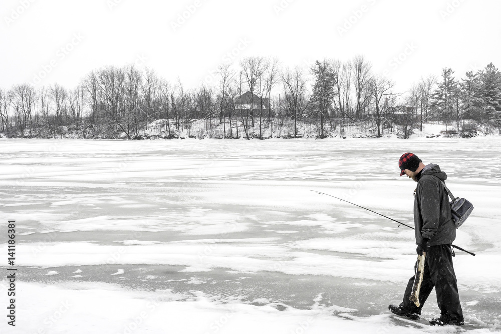 Outdoor fisherman walking across a frozen lake in winter carrying his gear and a log