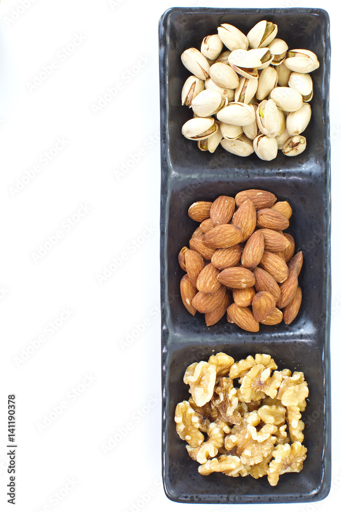 Assorted mixed nuts in black plate on white background Assorted mixed nuts in black plate on white background