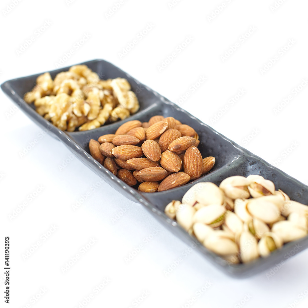 Assorted mixed nuts in black plate on white background Assorted mixed nuts in black plate on white background
