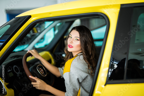 Beautiful Smiling woman driving yellow car, attractive girl sitting in automobile, portrait.