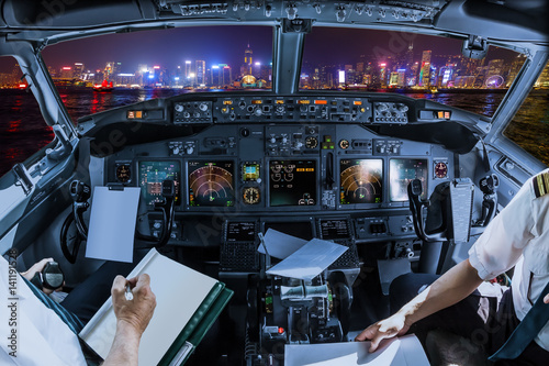 Airplane cockpit flying on Hong Kong panorama skyline with pilots arms and blank white papers for copy space.