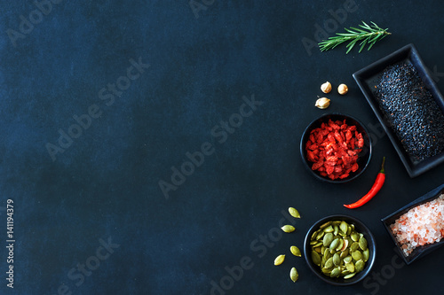 Black sesame, pumpkin seeds, dried tomato, himalayan salt, tarragon and cardamom. Spices and seasoning over black background with a copy space. 