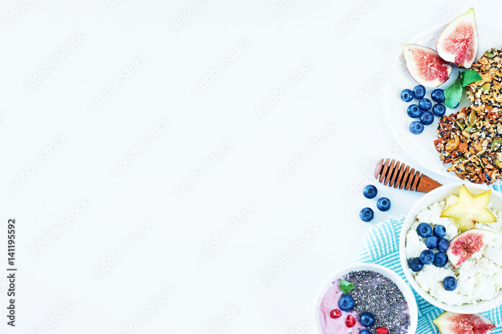 Top view of healthy breakfast dishes with a copy space. Yoghurt with chia, cottage cheese with figs, blueberry and carambola, wholegrain cookies on a white table. Top view of healthy breakfast dishes with a copy space. Yoghurt with chia, cottage cheese with figs, blueberry and carambola, wholegrain cookies on a white table.