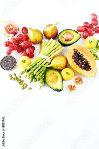 Vertical top view of fresh fruits  veggies  seeds and nuts over white board with empty space. Vegetarian background or clean eating concept. 