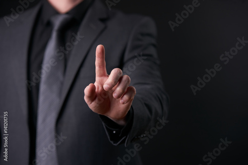 Businessman in trendy black suit using virtual touchscreen isolated on black background.Touch screen business futuristic concept, finger push interface, design template.