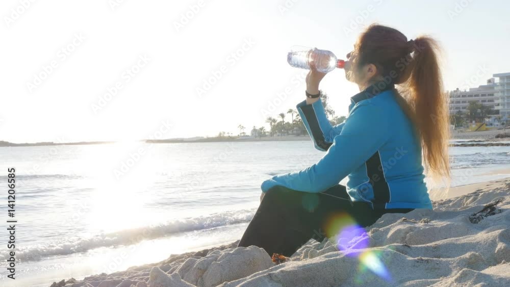 Young woman in sport clothes drinking water after workout on the beach Young woman in sport clothes drinking water after workout on the beach