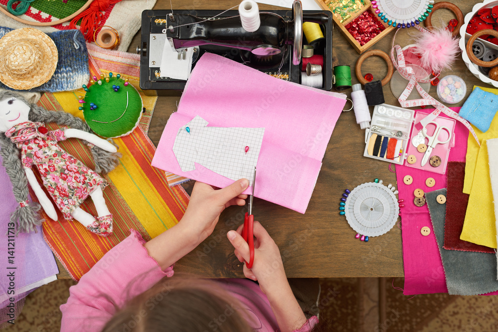 Fototapeta premium girl sews doll clothes, top view, sewing accessories top view, seamstress workplace, many object for needlework, handmade and handicraft