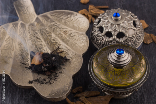 Silver Oriental Artisitc Arabian Oud Perfume / Arabian Oud Perfume with Oud Scented Wood burned in the background with Scented Smoke in the Air  © bassemadel