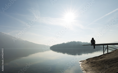 Enjoying nature, self-reflection. Woman sitting on the shore of the lake. Clear sunny day. Monochrome.