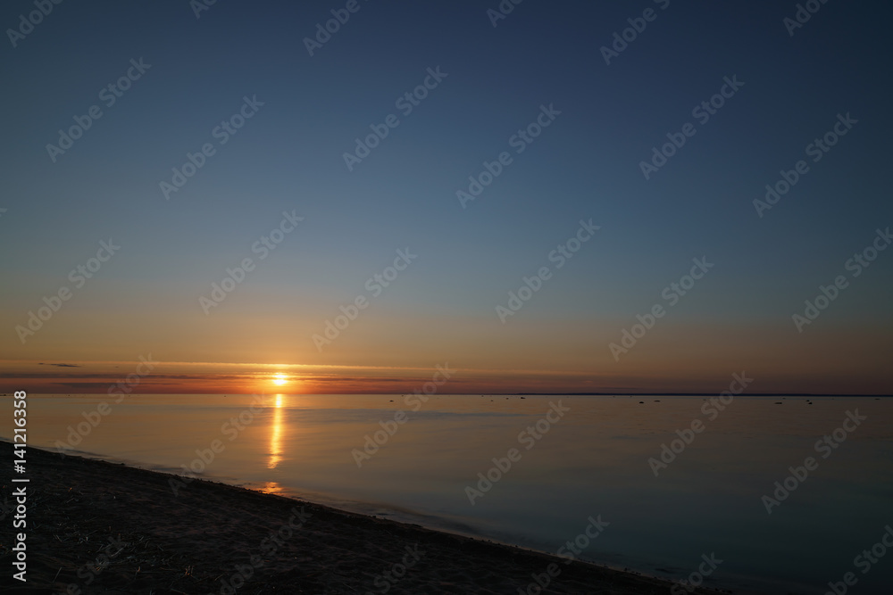 orange sunset over baltic sea with clear sky and clouds near sun, summertime photo