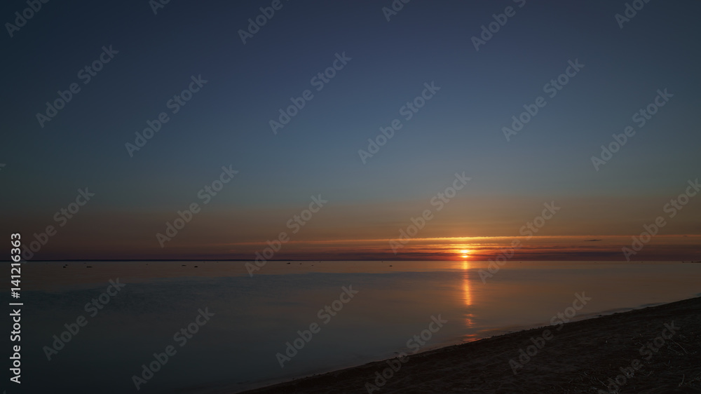 orange sunset over baltic sea with clear sky and clouds near sun, summertime photo