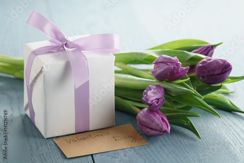 Fototapeta Naklejka Na Ścianę i Meble -  white gift box with purple bow and tulips on blue wood background, valentines day paper card