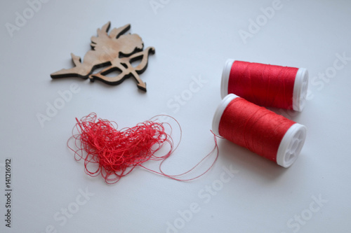 Heart in shape of red buttons, needle and yarn on unbleached fabric.