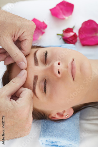 Beautiful young girl having face massage in spa salon.