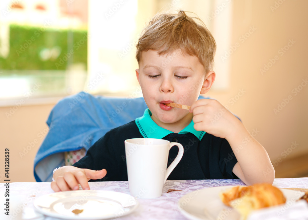 Small blond boy enjoys his breakfast, sitting at a table in a resort cafe. Small blond boy enjoys his breakfast, sitting at a table in a resort cafe.