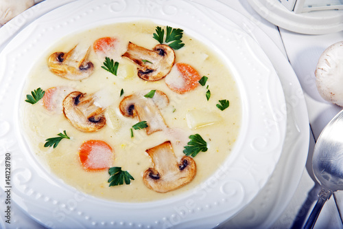 Champignon soup with parsley, carrots and potatoes on a white wooden table