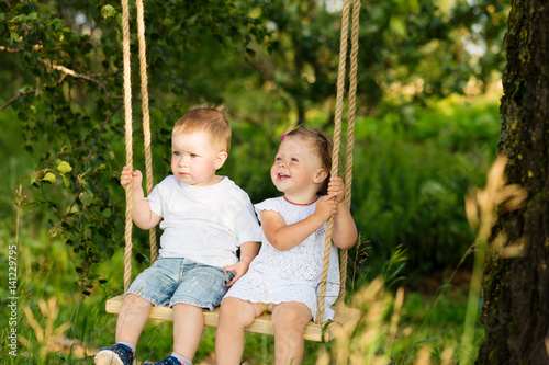 Two small children are riding on a swing outdoors