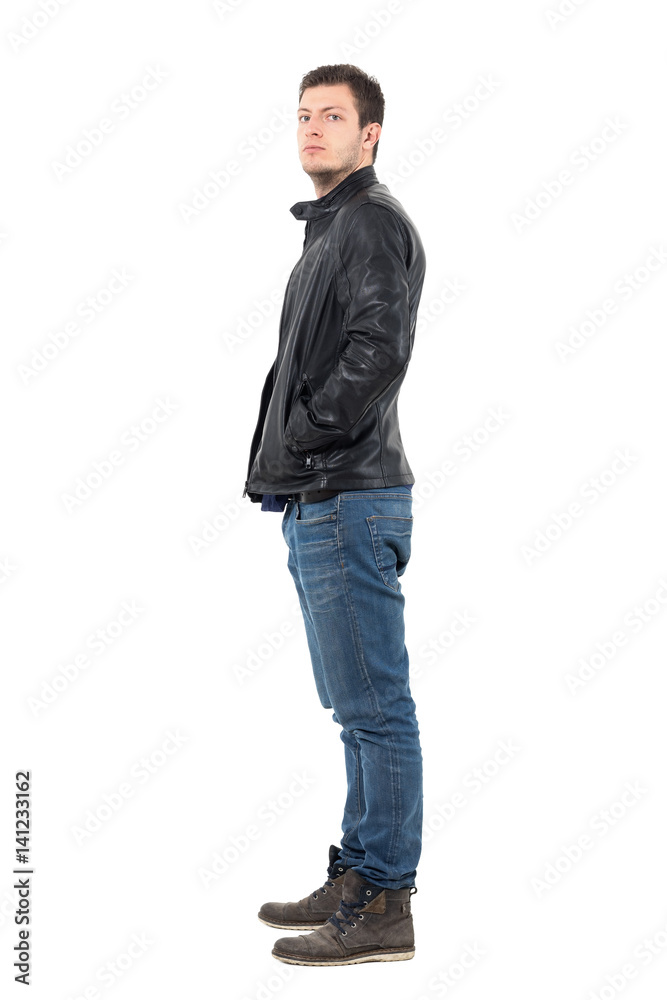 Side view of serious confident macho man with hands in pockets looking at camera. Full body length portrait isolated over white studio background. Side view of serious confident macho man with hands in pockets looking at camera. Full body length portrait isolated over white studio background.
