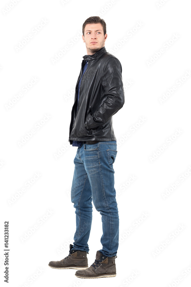 Side view of young man in leather jacket and jeans looking back over the shoulder. Full body length portrait isolated over white studio background. Side view of young man in leather jacket and jeans looking back over the shoulder. Full body length portrait isolated over white studio background.