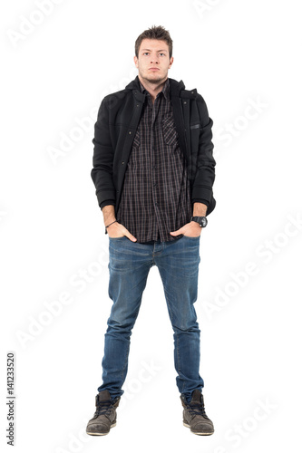 Serious young man in winter jacket and leather ankle boots looking at camera. Full body length portrait over white studio background.